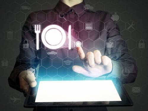 A person holding a tablet with glowing fork, plate, and restaurant service icons hovering above the screen.